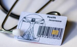 A person holding a debit card next to a stack of medical bills and prescription bottles on a kitchen counter.